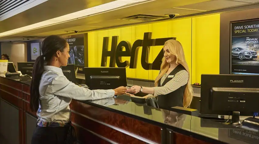 Een vrouw overhandigt iets aan de Hertz autohuur balie
